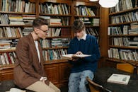 Two students engaging in study at a library, surrounded by books, focusing on learning.